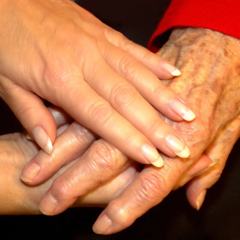 Zwei helfende Hände legen sich behutsam um die Hand einer älteren Person – Nahaufnahme als Symbol für Fürsorge, Vertrauen, menschliche Nähe